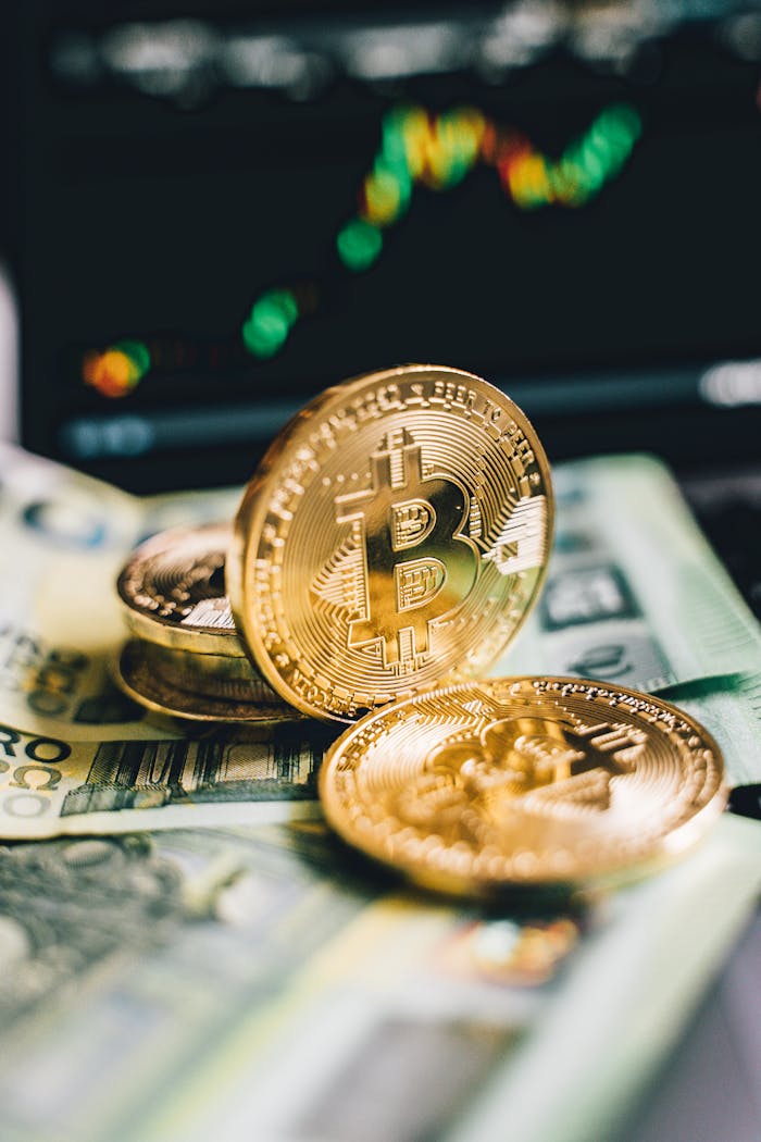 Close-up of golden Bitcoin coins on banknotes with a blurred cryptocurrency graph background.